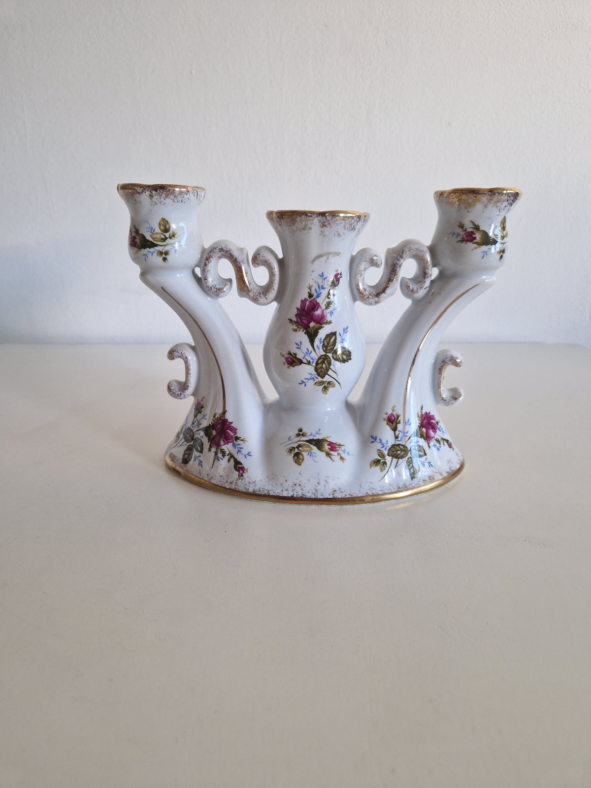Vintage white porcelain three-arm candelabra with floral rose patterns and gold trim.