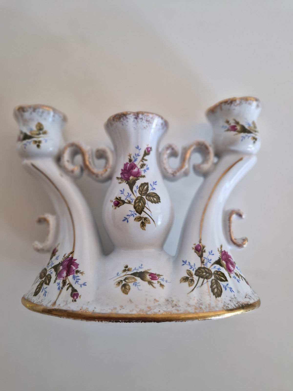 Vintage white porcelain three-arm candelabra with pink rose floral patterns and gold trim.
