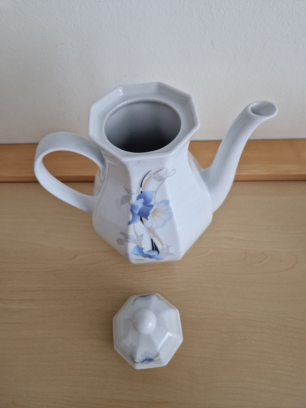 Vintage white porcelain teapot with blue flower pattern and detached lid on a wooden surface