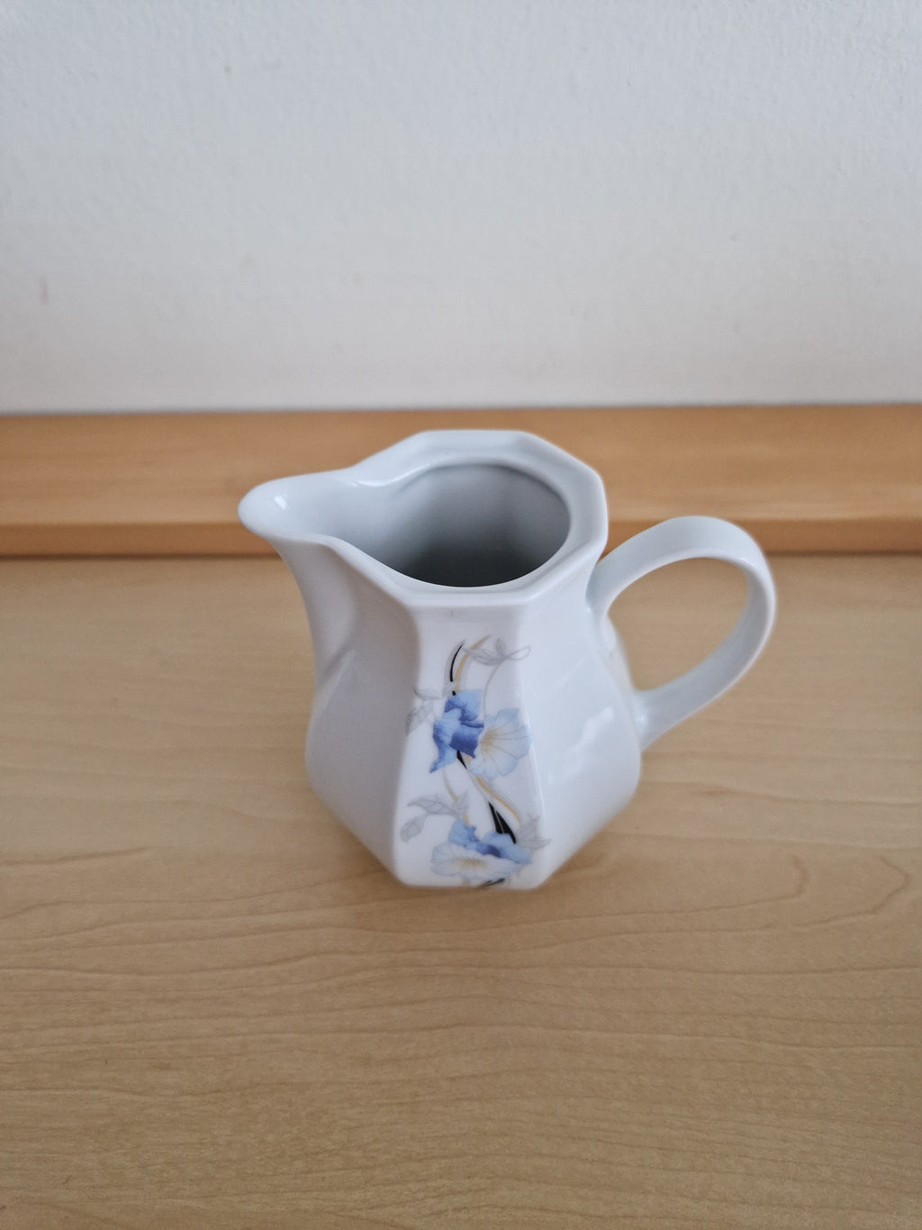 Vintage white porcelain creamer pitcher with blue floral pattern on a light wooden surface