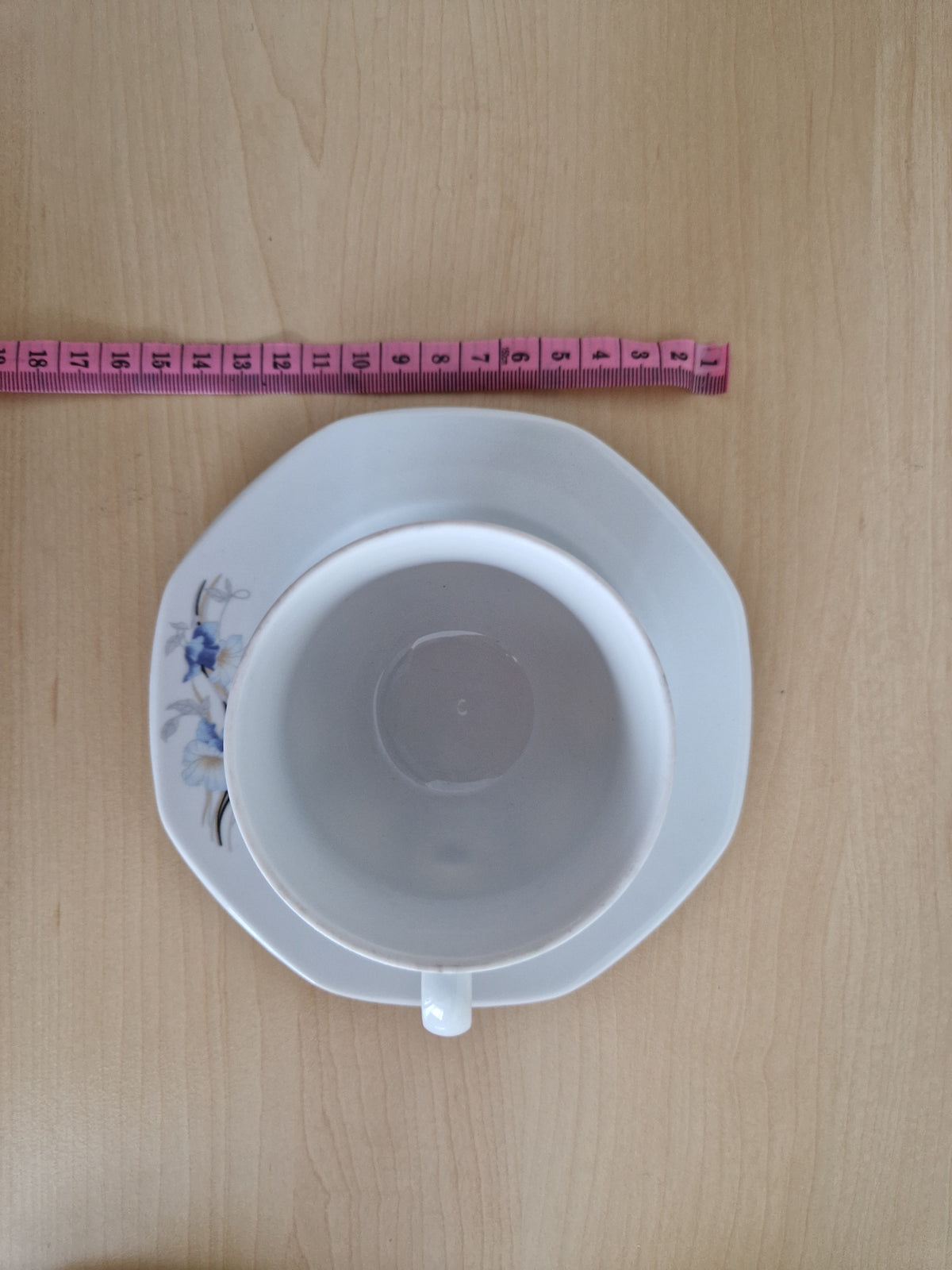 Top view of a white vintage porcelain tea cup and saucer with blue floral details.
