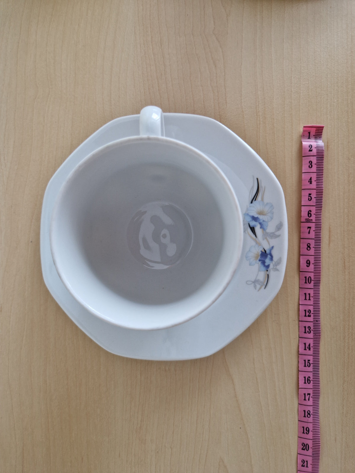Vintage white porcelain teacup and saucer with blue floral pattern and measuring tape