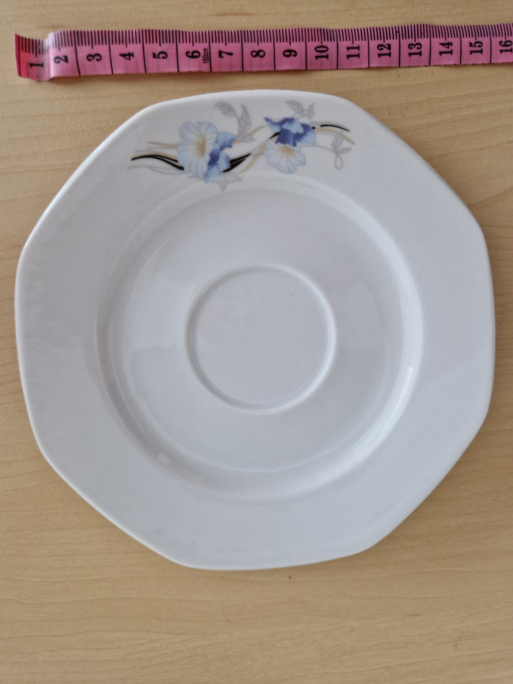 Vintage white porcelain saucer with blue floral design and pink measuring tape.