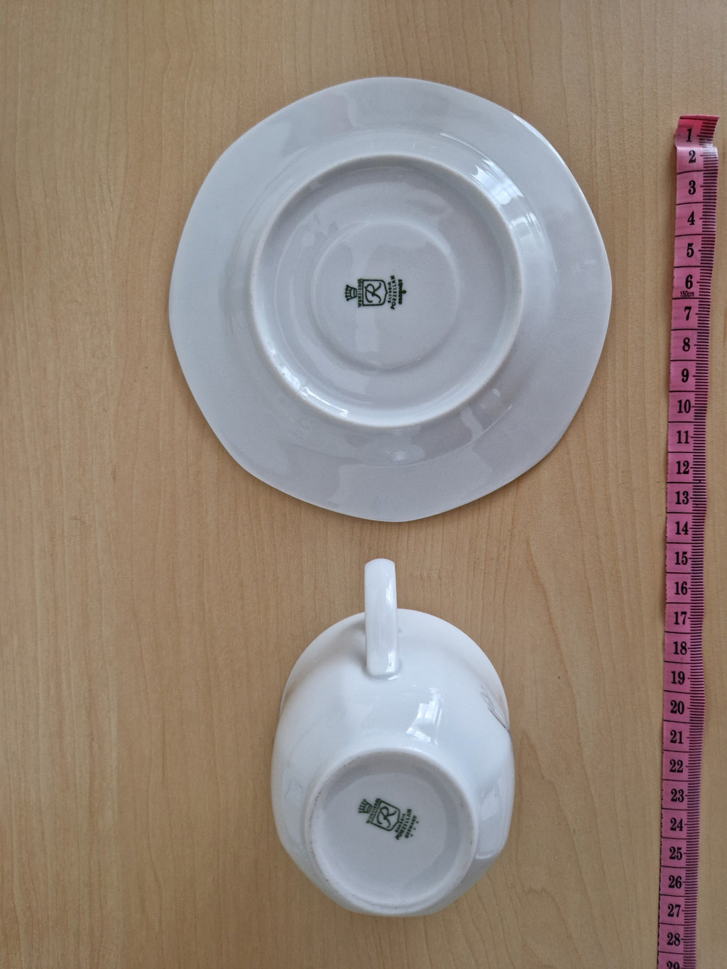 Bottom view of a vintage white porcelain teacup and saucer with brand marks and measuring tape.
