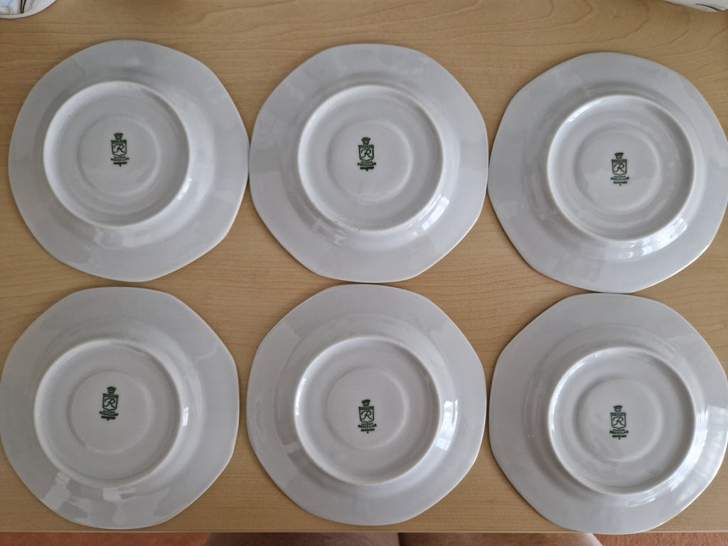 Set of six vintage white porcelain plates showing underside maker's marks on a wooden surface.