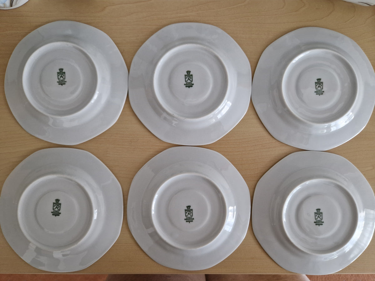 Set of six vintage white porcelain plates showing underside maker's marks on a wooden surface.