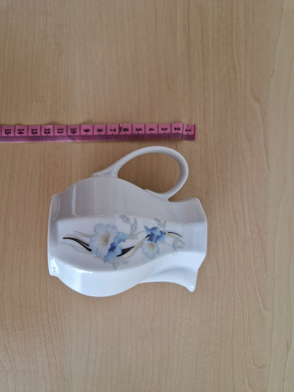 Vintage white porcelain creamer with blue floral pattern and curved handle.