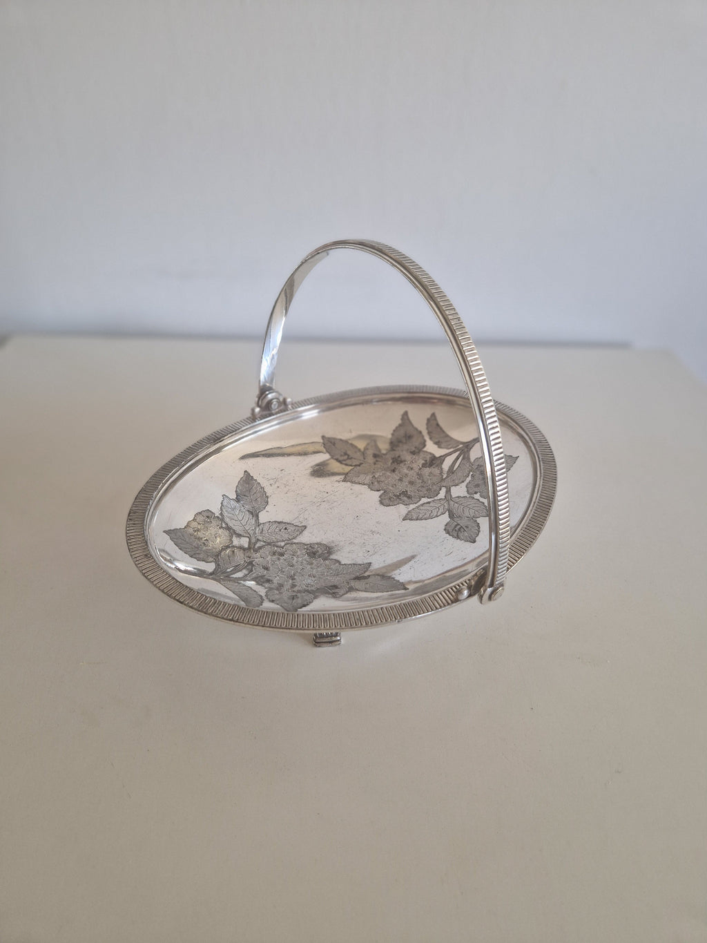 Angled view of antique Meriden silver-plated Victorian basket showing feet and rim detail