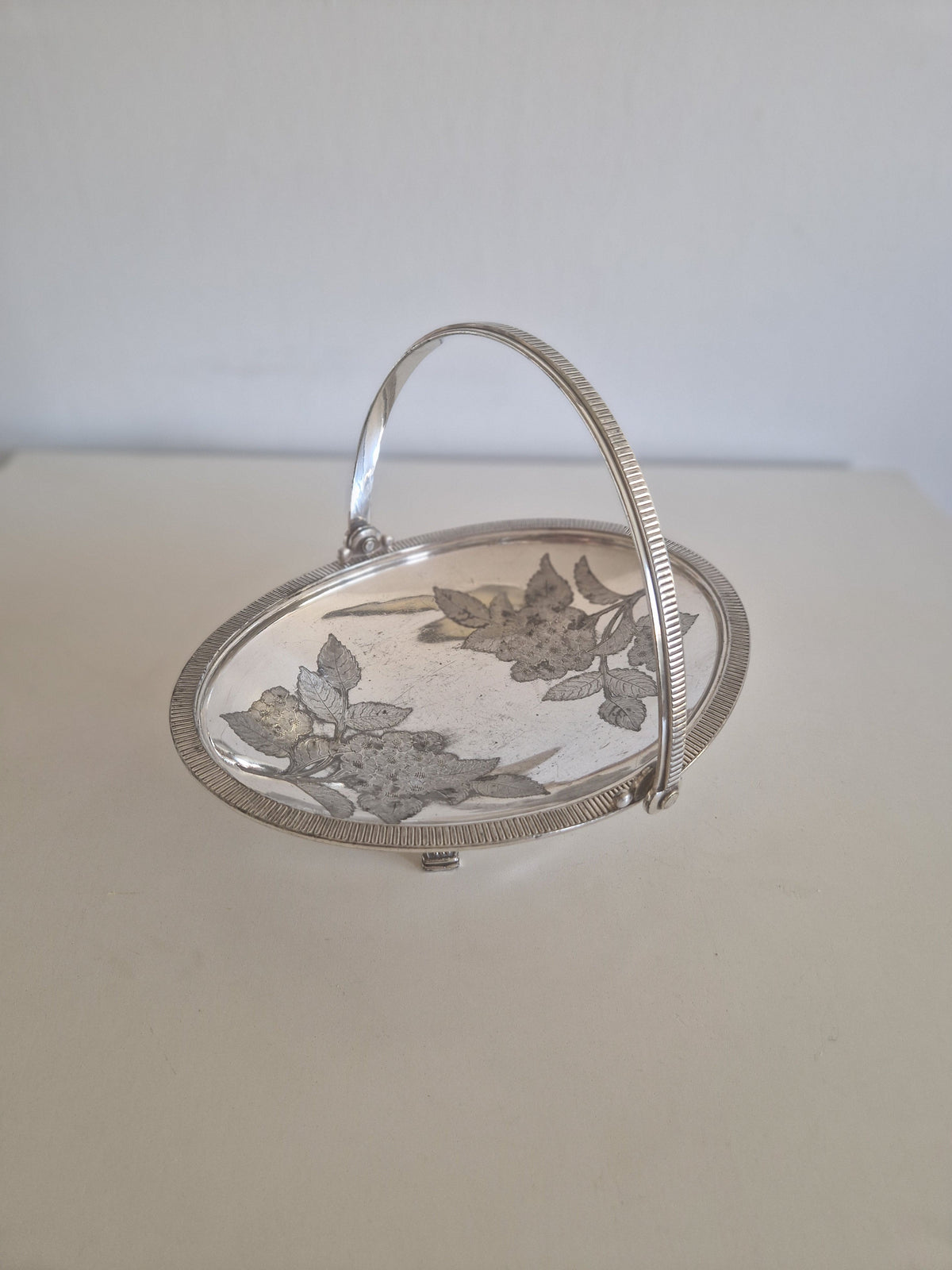 Angled view of antique Meriden silver-plated Victorian basket showing feet and rim detail