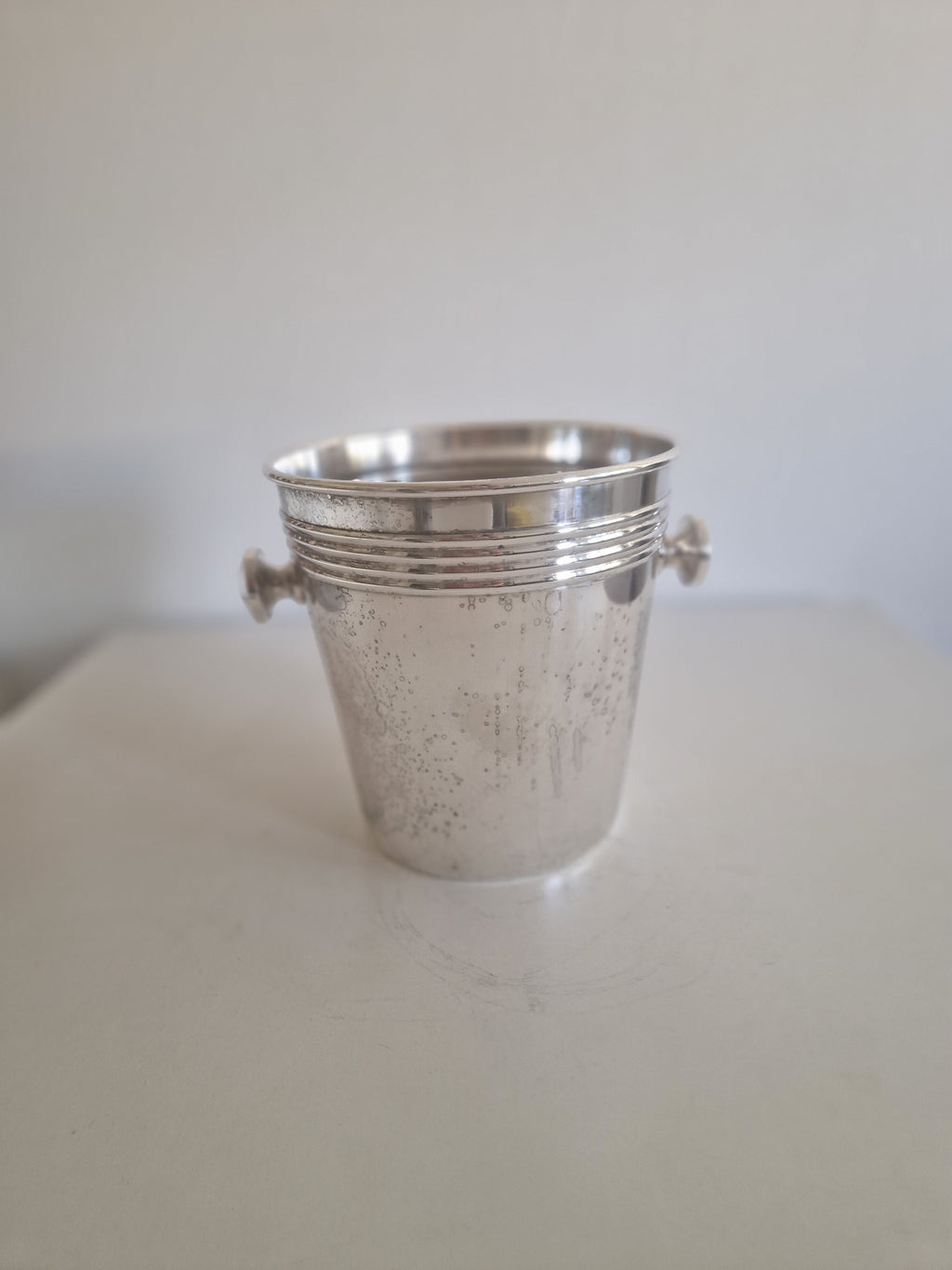 Vintage silver ice bucket with decorative handles on a white surface.