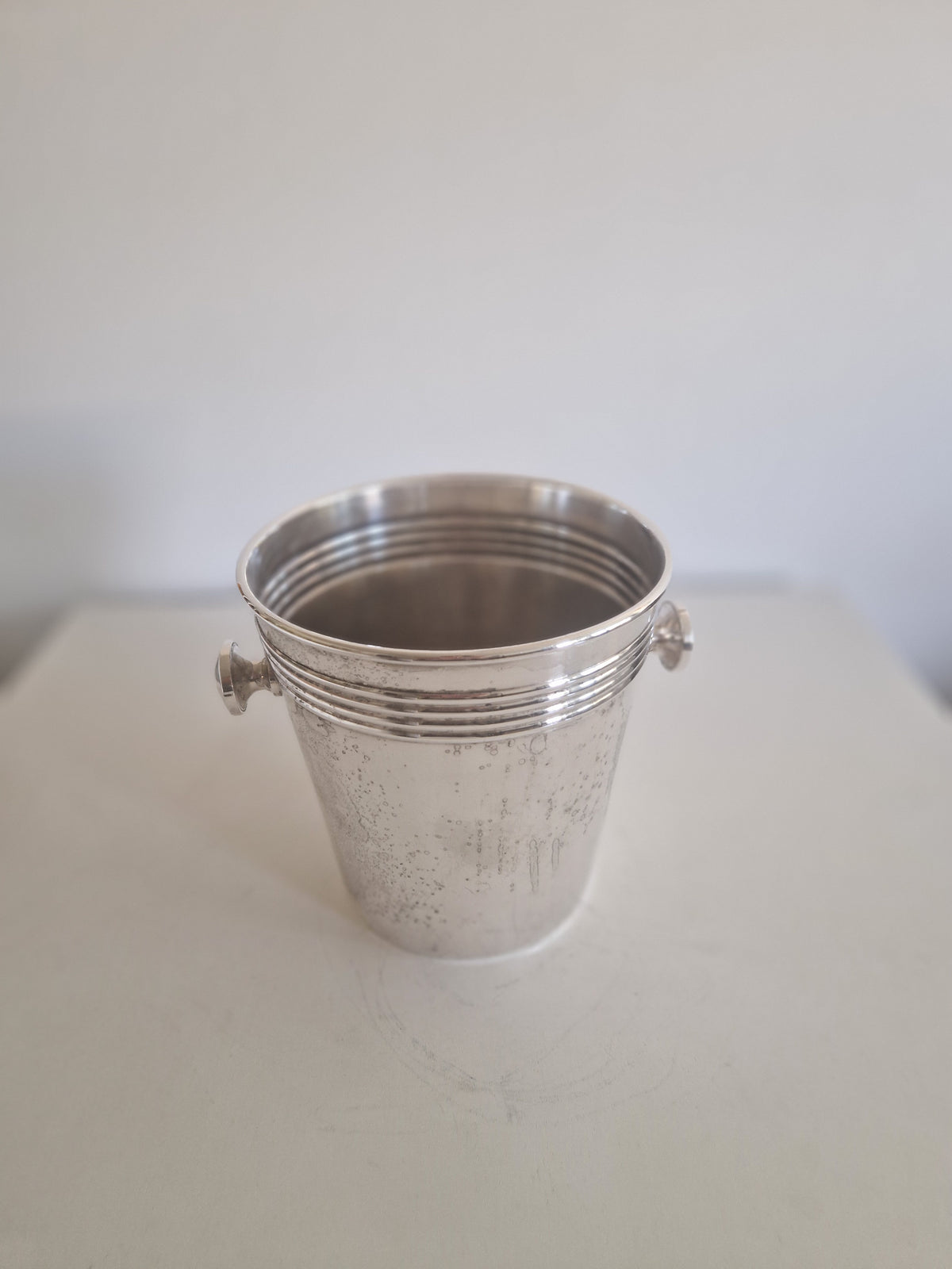 Vintage silver metal bucket with ribbed texture and small side handles on a white surface.