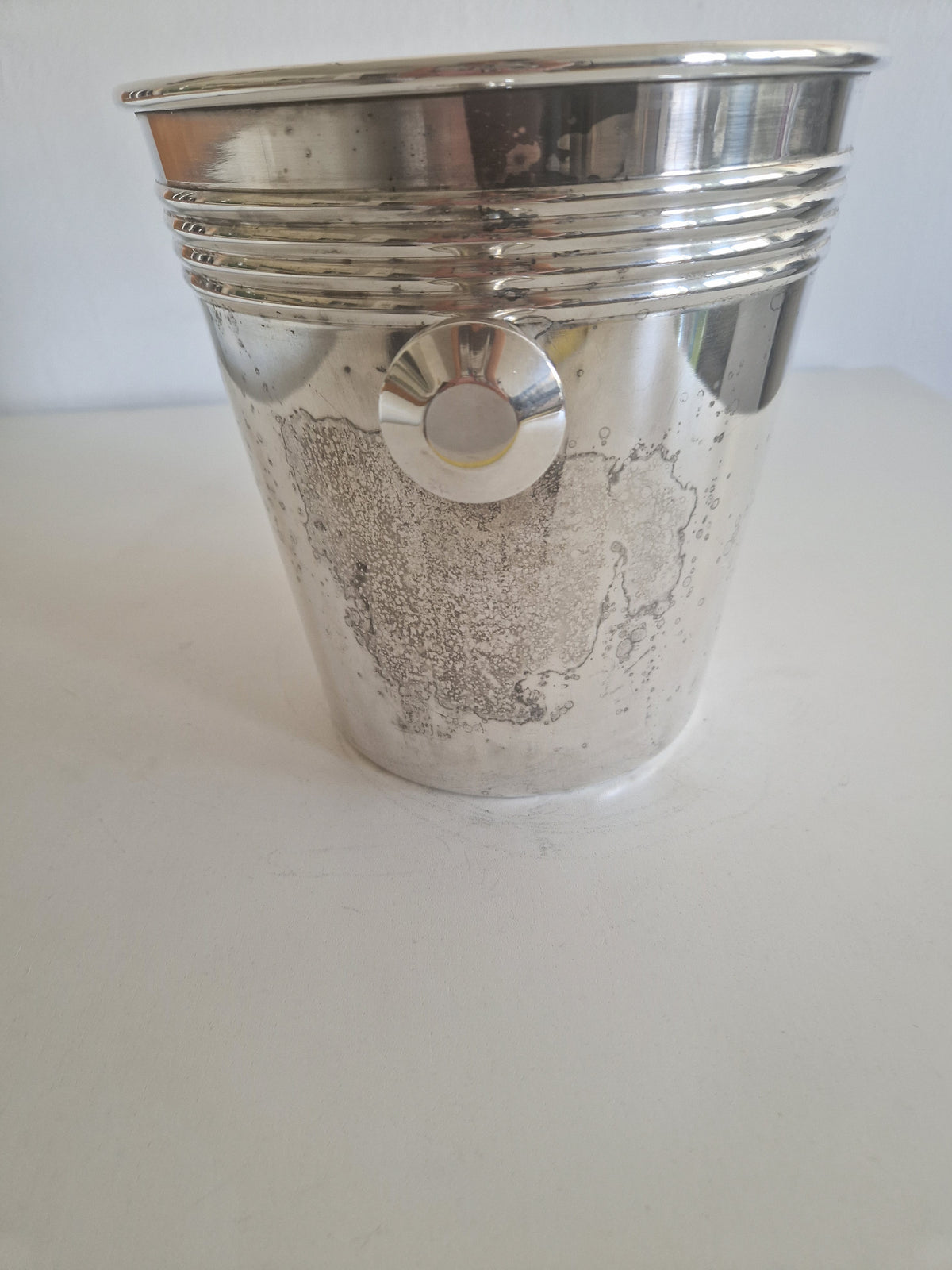 Vintage silver-plated champagne bucket with decorative ribbed detailing on a white surface.
