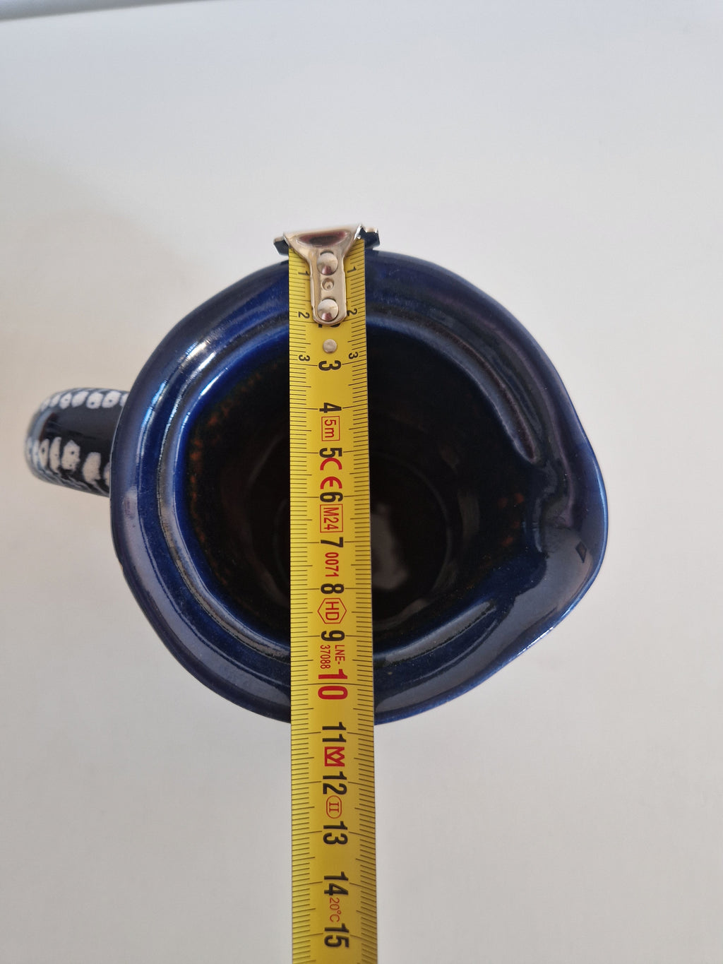 Top view of a blue ceramic vessel being measured with a yellow tape measure.