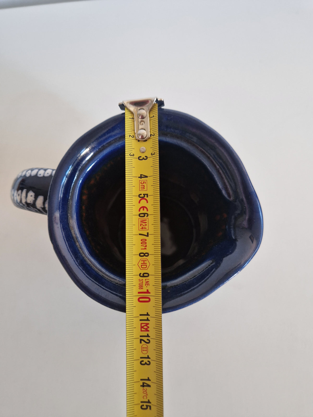 Top view of a blue ceramic vessel being measured with a yellow tape measure.