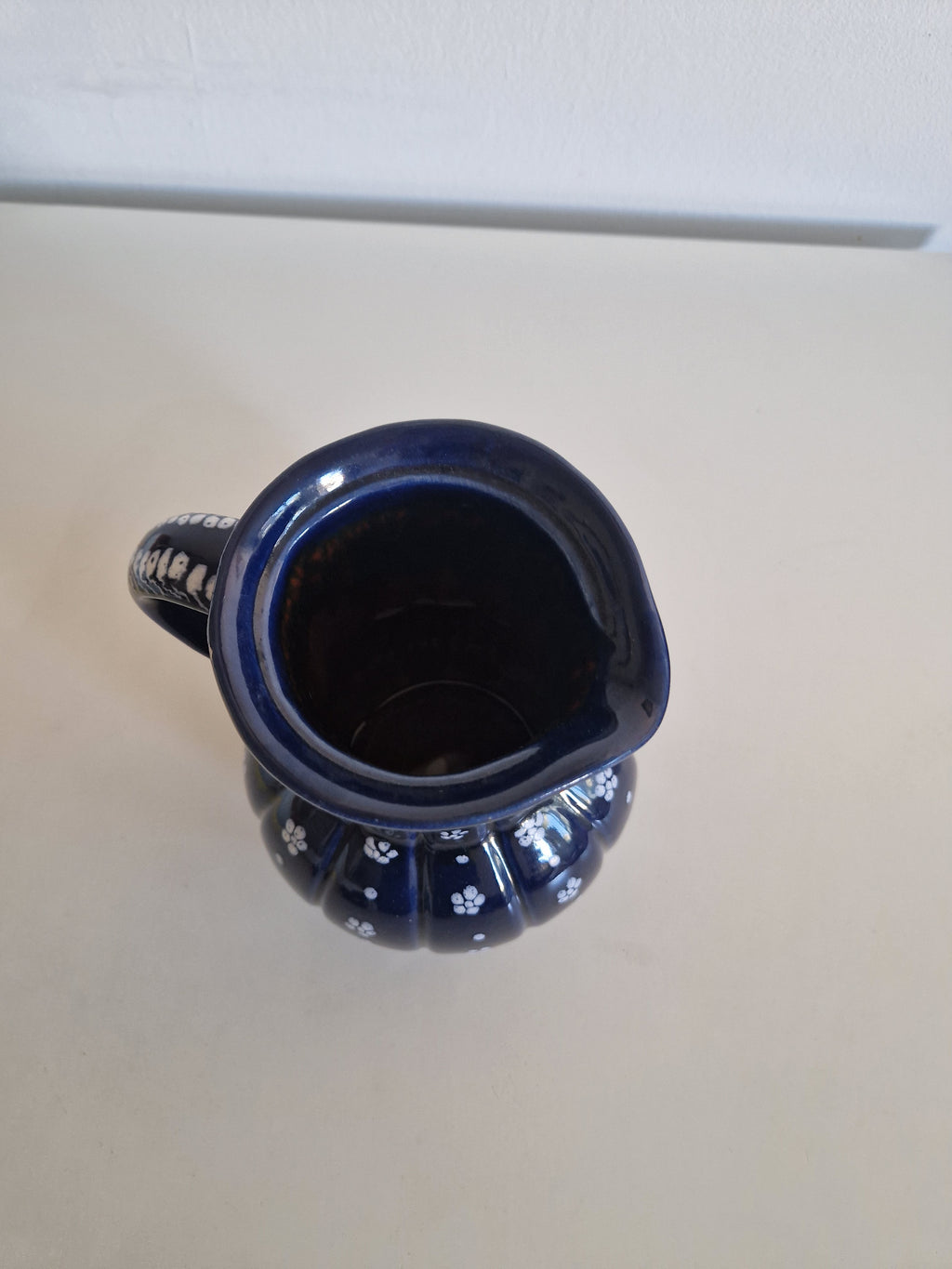 Vintage dark blue ceramic pitcher with white floral patterns and a handle.