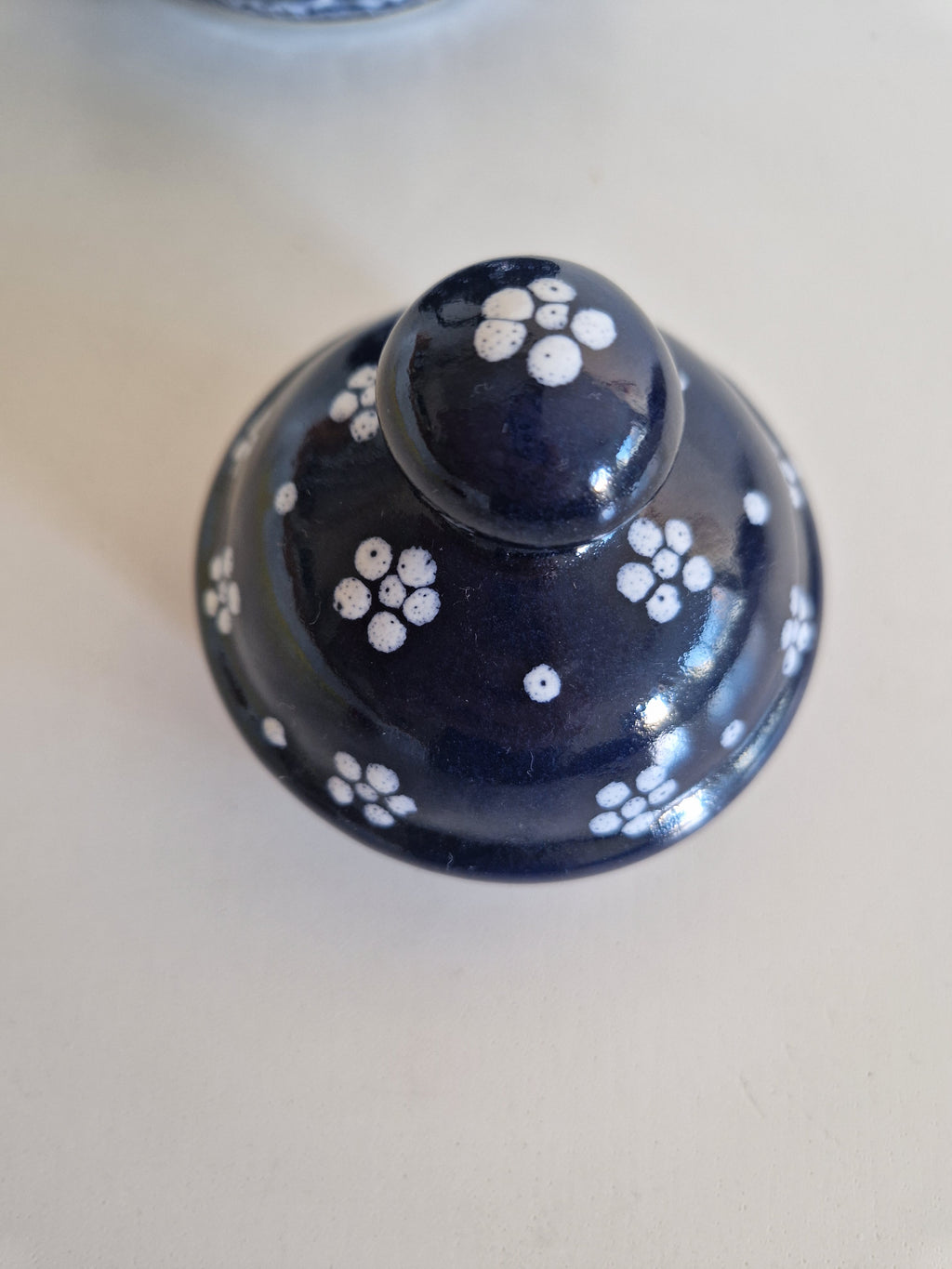 Vintage dark blue porcelain lid with white floral patterns and a round knob.
