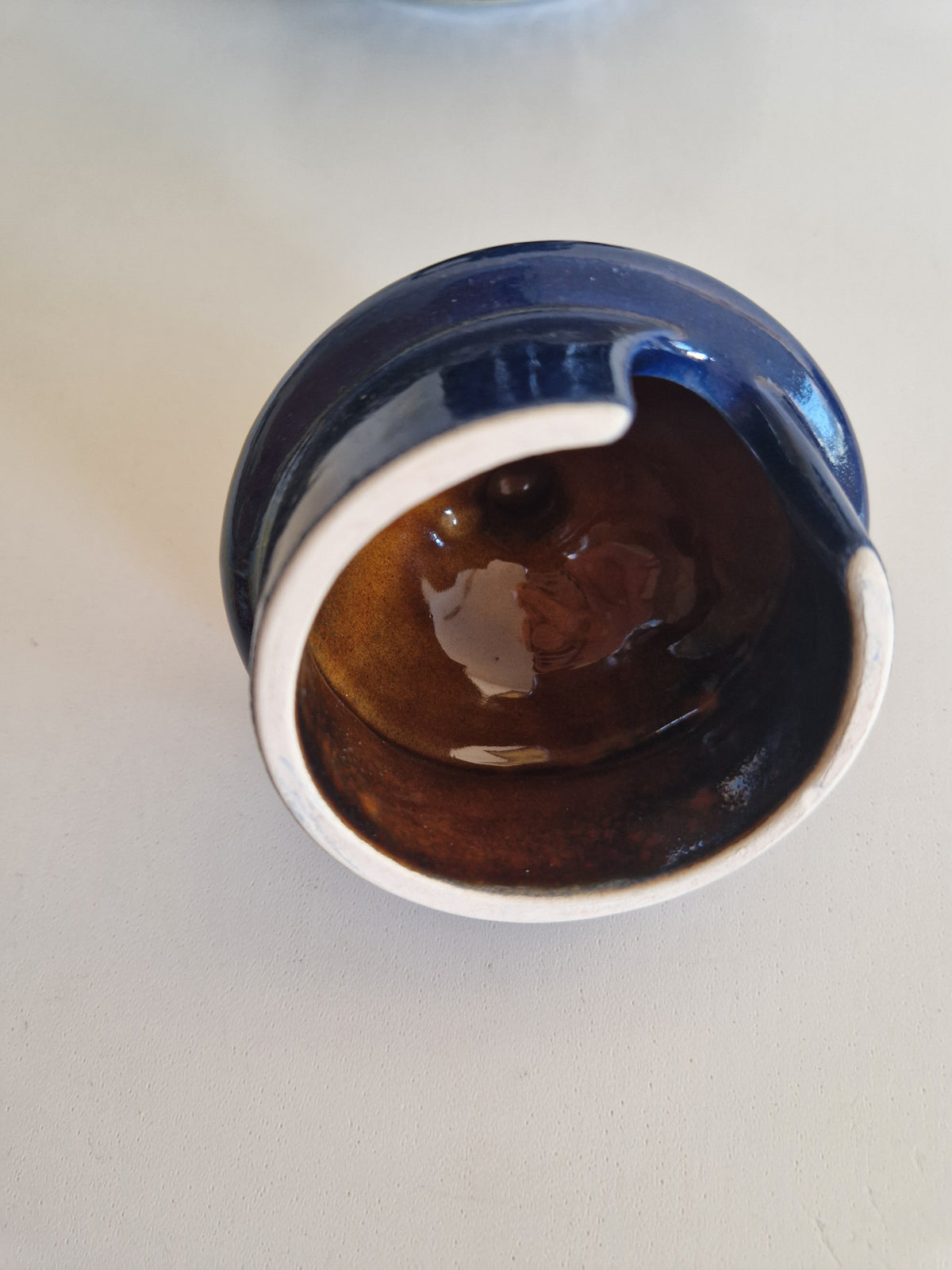 Top view of a vintage blue glazed ceramic bowl with a brown interior on a white surface.