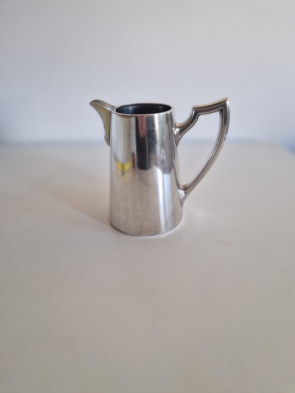 Vintage silver pitcher with elegant handle on a white surface.