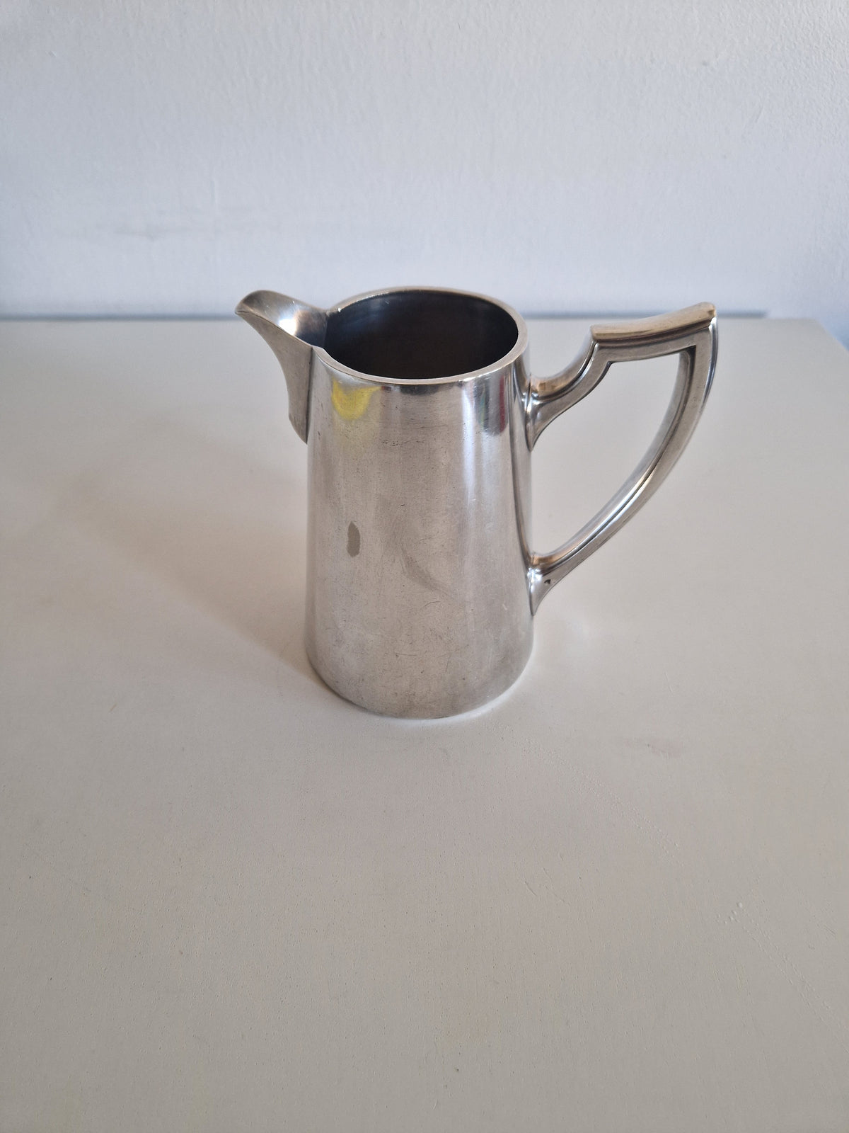 Vintage silver pitcher with a sleek handle and spout on a white surface