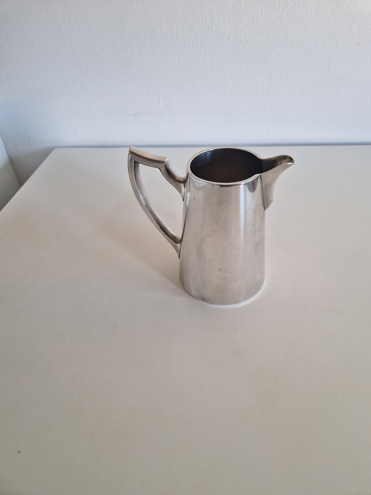 Vintage silver pitcher with a sleek handle and spout on a white surface.