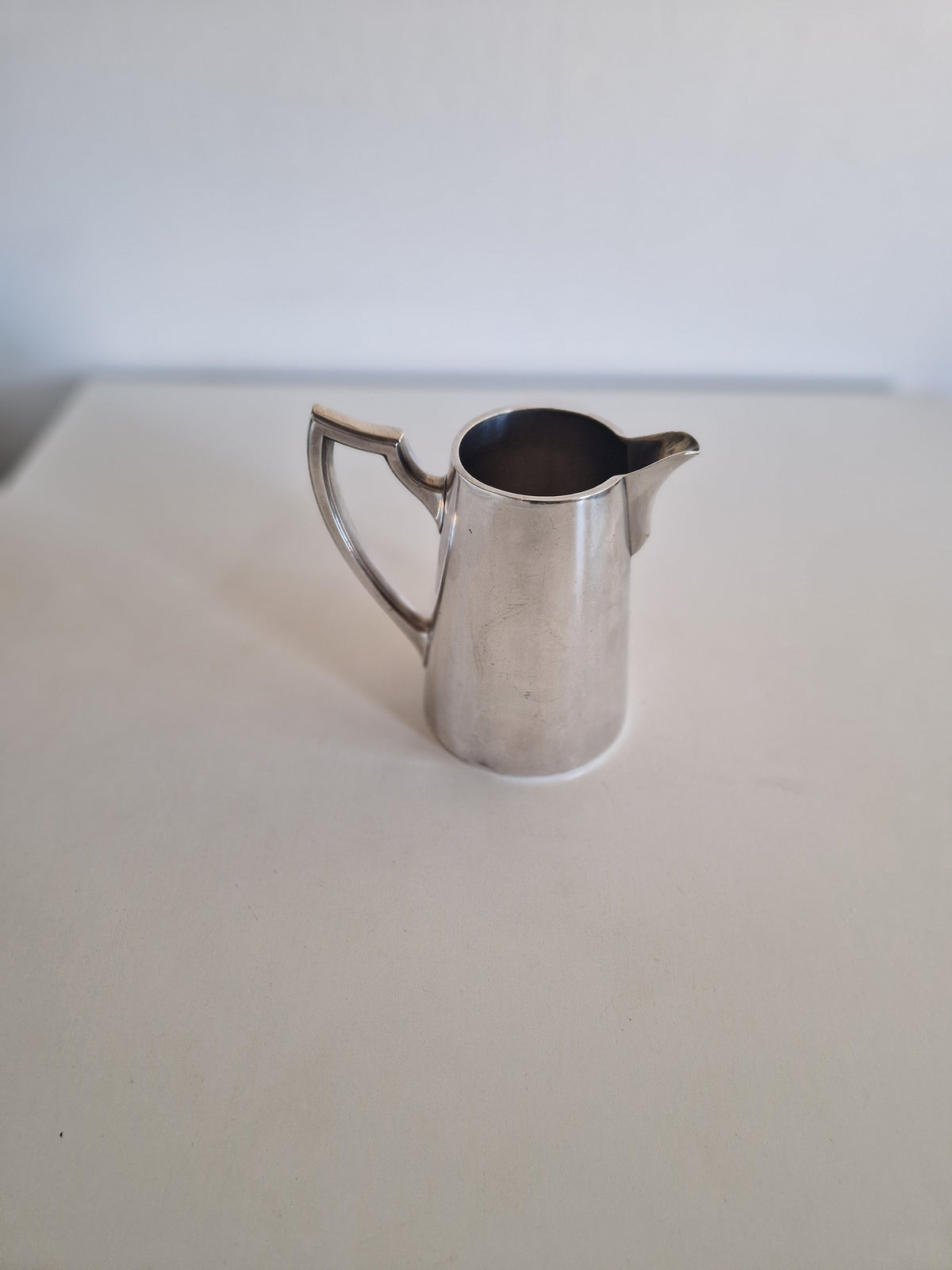 Vintage silver pitcher with a sleek handle and spout on a white surface.