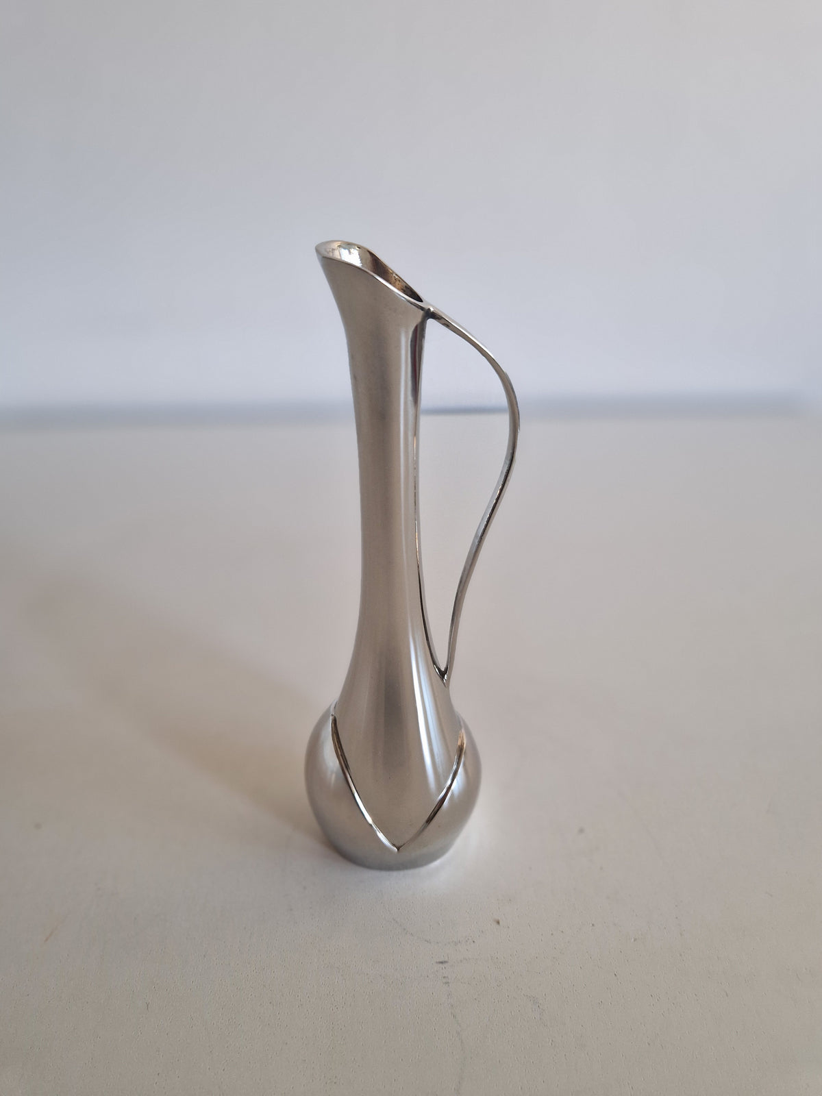 Elegant vintage silver pitcher with a slender neck and curved handle on a white surface.