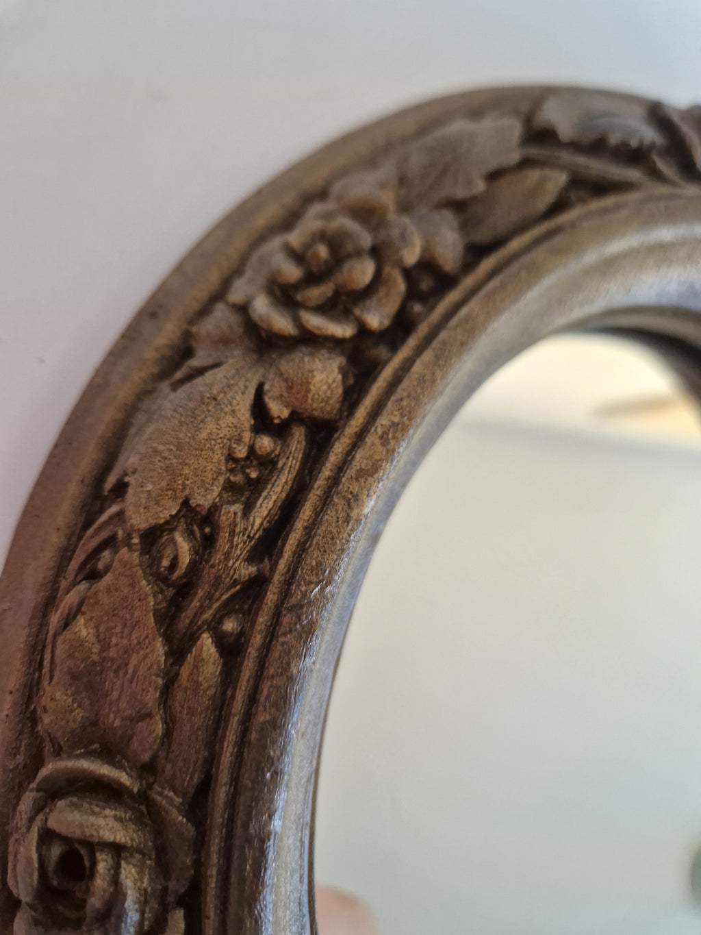 Close-up of a vintage carved wooden mirror frame with intricate floral rose details.
