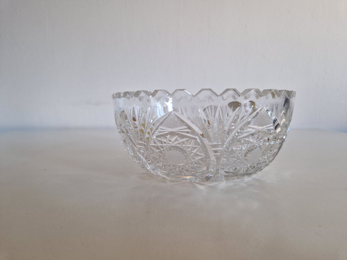 Vintage cut crystal glass bowl with intricate geometric patterns on a white surface.